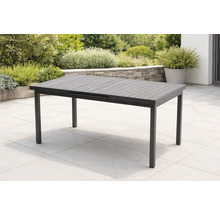 Table de jardin extensible moderne gris foncé sur une terrasse en pierre claire, entourée de plantes et d'un muret en pierre naturelle.