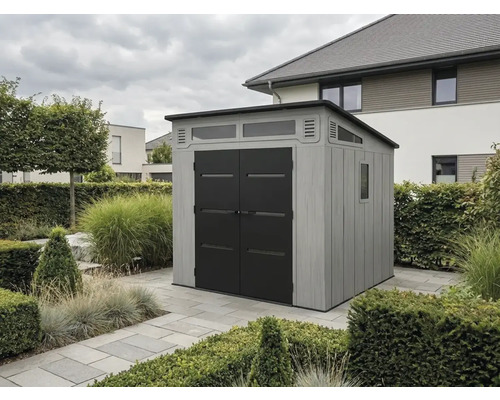 Abri de jardin moderne avec parois grises aspect bois, doubles portes noires et fenêtres, situé sur des dalles en pierre dans un jardin.
