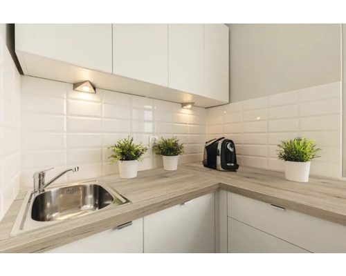 Moderne Küche mit heller Arbeitsplatte in Holzoptik, Edelstahlspüle, weißen Metro-Fliesen und Unterbauleuchten.
