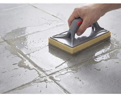 Nettoyage de carreaux de sol avec une taloche éponge à poignée grise et éponge jaune après le jointoiement.