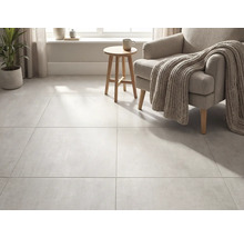 Großformatige Bodenfliesen in Betonoptik in einem hellen Wohnzimmer mit Sessel, Strickdecke und Holzbeistelltisch.