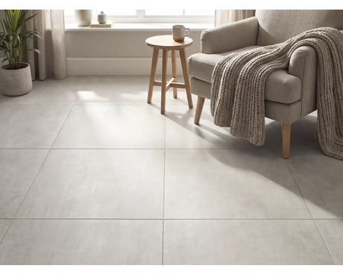 Großformatige Bodenfliesen in Betonoptik in einem hellen Wohnzimmer mit Sessel, Strickdecke und Holzbeistelltisch.