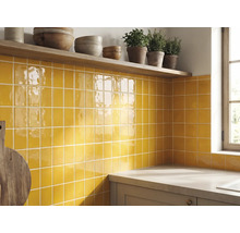 Küchenrückwand mit gelben glänzenden quadratischen Wandfliesen, einem Holzregal mit Schüsseln und Kräutern sowie einer Arbeitsplatte.