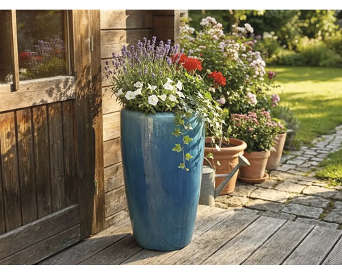 Grand pot de fleurs bleu en céramique planté de lavande et de géraniums sur une terrasse en bois à côté d'un abri de jardin en bois.