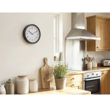 Helle Küche mit einer runden Wanduhr an der Wand, Holzschneidebrett, Kräutertopf und Aufbewahrungsgläsern auf der Arbeitsplatte.
