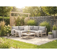 Eck-Gartenlounge aus Holz mit grauen Polstern, Holztisch und Teppich auf einer hellen Steinterrasse umgeben von Gräsern und Gabionenwand.