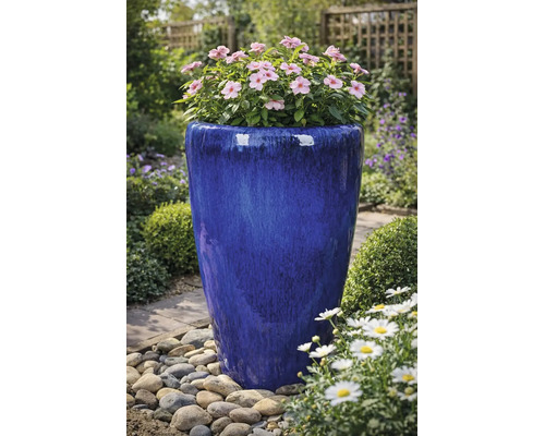 Grand pot de fleurs en céramique émaillée bleue avec des fleurs roses dans un jardin avec des galets.