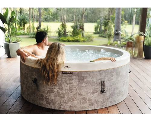 Spa gonflable MSpa avec deux personnes sur une terrasse en bois dans un jardin lumineux.