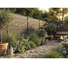 Jardin moderne avec clôture grise, pavés en pierre naturelle, plantes en pots en terre cuite, guirlande lumineuse et brasero allumé.