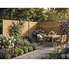 Scène de jardin avec clôture pare-vue en bois, mobilier en bois, plantes à fleurs comme la lavande et les hortensias, et guirlandes lumineuses.
