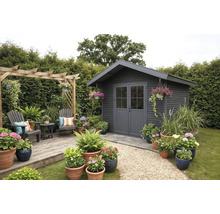 Abri de jardin moderne en bois anthracite avec double porte, terrasse en bois avec coin salon, pergola et nombreux pots de fleurs.