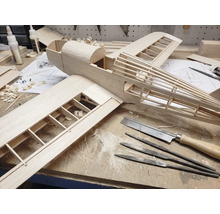 Construction d'un modèle réduit d'avion en bois sur un établi avec des outils comme une scie fine, des limes aiguilles et de la colle à bois.