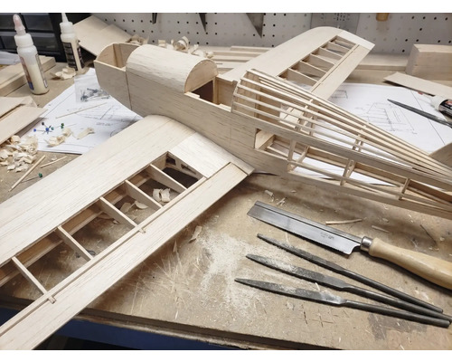 Construction d'un modèle réduit d'avion en bois sur un établi avec des outils comme une scie fine, des limes aiguilles et de la colle à bois.