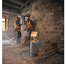 Chauffage radiant à gaz sur une bouteille de gaz sur un chantier avec des ouvriers devant un mur en briques.