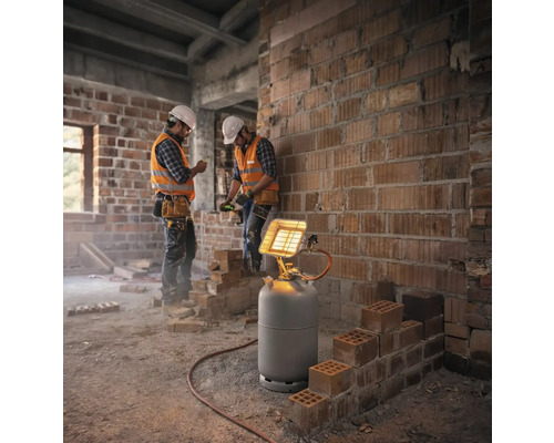 Chauffage radiant à gaz sur une bouteille de gaz sur un chantier avec des ouvriers devant un mur en briques.