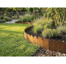 Gewellte Rasenkante aus Metall in Rost-Optik trennt ein bepflanztes Beet von einer Rasenfläche in einem hellen Garten.