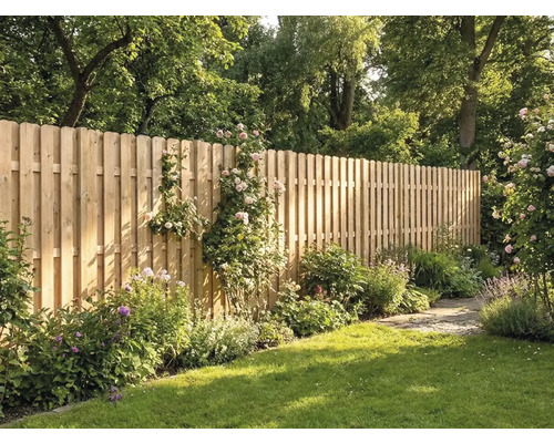 Hoher Holzzaun aus vertikalen Latten mit abgerundeten Köpfen in einem sonnigen Garten mit Rasen, Blumen und Bäumen.