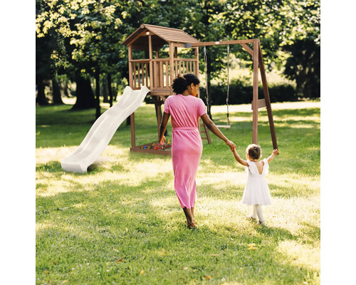 Aire de jeux en bois avec toboggan, balançoire, cabane et bac à sable dans un jardin lumineux avec une femme et un enfant.