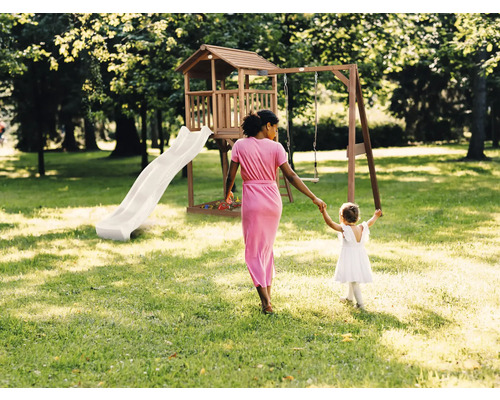 Tour de jeux en bois avec toboggan et balançoire dans un jardin lumineux avec une femme et un enfant.