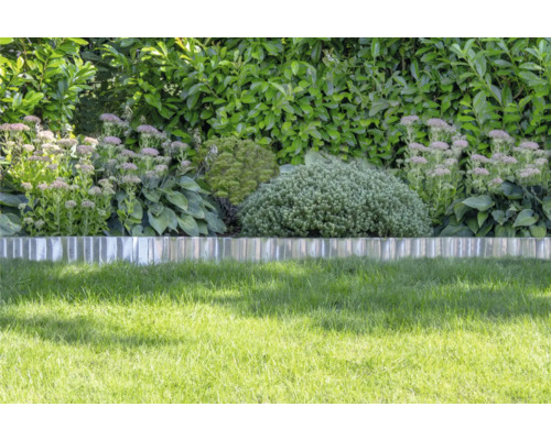 Bordure de pelouse en métal séparant le gazon d'un massif de vivaces et d'arbustes devant une haie.