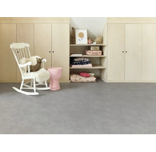 Helles Kinderzimmer mit grauem Bodenbelag in Betonoptik, weißem Schaukelstuhl und Einbauschränken aus hellem Holz.