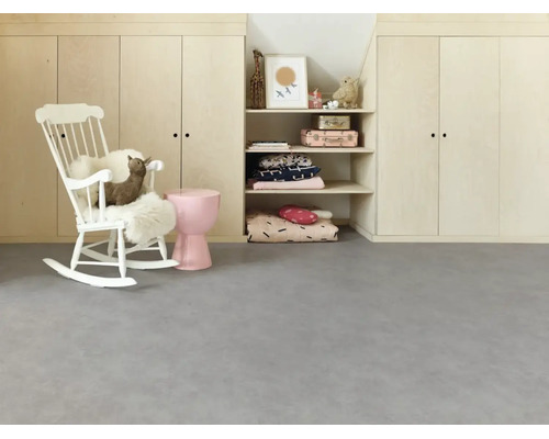 Helles Kinderzimmer mit grauem Bodenbelag in Betonoptik, weißem Schaukelstuhl und Einbauschränken aus hellem Holz.