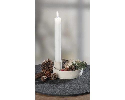 Brennende weiße Stabkerze in weißem Halter, dekoriert mit Tannenzapfen, Rinde und Tannenzweig auf grauem Filzuntersetzer.