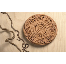 Runde Ton-Dekoration mit Spiralmustern und Relief-Verzierungen auf einer Holzoberfläche neben einem gewundenen Ast.