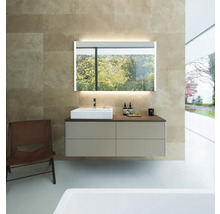 Modernes Badezimmer mit hängendem Waschtischunterschrank, weißem Aufsatzbecken und beleuchtetem Spiegel vor beiger Fliesenwand.