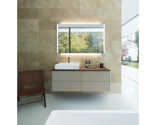 Modernes Badezimmer mit hängendem Waschtischunterschrank, weißem Aufsatzbecken und beleuchtetem Spiegel vor beiger Fliesenwand.