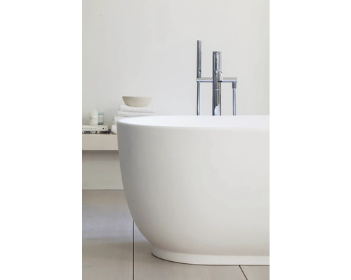 Baignoire îlot ovale avec robinetterie sur pied en chrome et douchette dans une salle de bains moderne et lumineuse.
