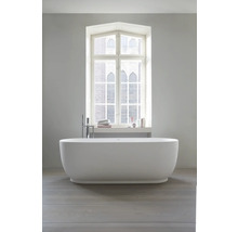 Baignoire îlot blanche dans une salle de bain moderne et lumineuse devant une fenêtre, robinetterie au sol, parquet.