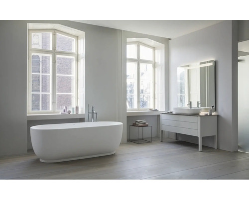 Salle de bains moderne et lumineuse avec baignoire en îlot robinetterie sur pied meuble sous vasque et grand miroir éclairé