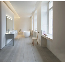 Salle de bains minimaliste et lumineuse avec baignoire en îlot blanche, double vasque à poser et parquet en bois clair.