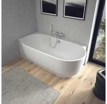 Baignoire îlot ovale moderne dans une salle de bain lumineuse avec parquet et murs aspect béton.