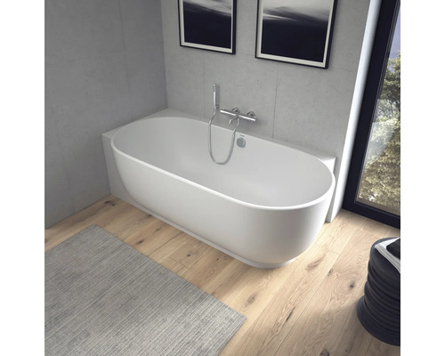 Baignoire îlot ovale moderne dans une salle de bain lumineuse avec parquet et murs aspect béton.