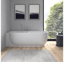 Baignoire moderne devant un mur en béton avec robinetterie chromée, parquet en bois et grande fenêtre sur le jardin.