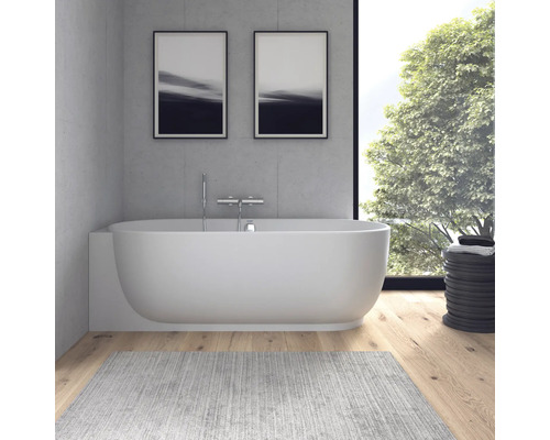 Baignoire moderne devant un mur en béton avec robinetterie chromée, parquet en bois et grande fenêtre sur le jardin.