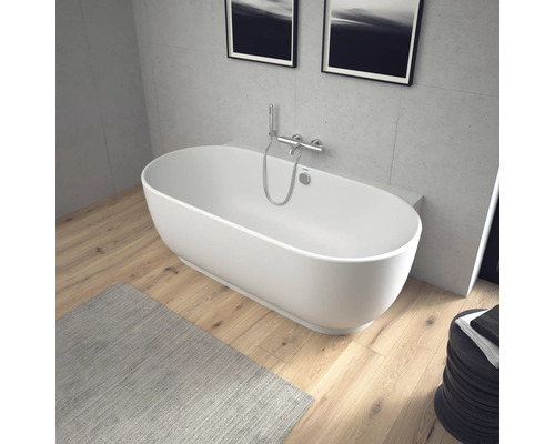 Baignoire îlot ovale avec robinetterie murale en chrome dans une salle de bains moderne avec sol en bois et murs aspect béton.
