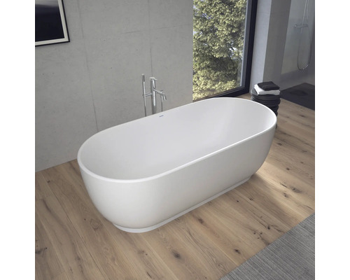 Baignoire îlot ovale dans une salle de bains moderne avec parquet, mur en béton et mitigeur sur pied.