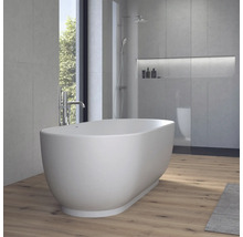 Baignoire îlot ovale dans une salle de bains moderne avec des murs aspect béton, un sol en bois et une douche à l'arrière-plan.