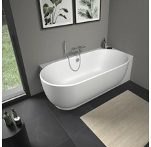 Baignoire en îlot blanche moderne de forme ovale dans une salle de bains lumineuse avec robinetterie murale chromée et carrelage foncé.