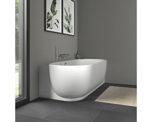 Baignoire murale ovale blanche moderne avec robinetterie chromée dans une salle de bain minimaliste avec sol carrelé et décoration murale.