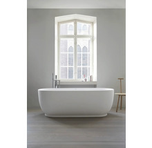 Baignoire îlot ovale avec robinetterie sur pied devant une grande fenêtre dans une salle de bains moderne et lumineuse.
