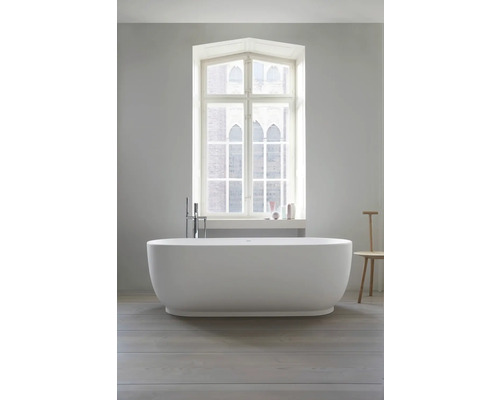 Baignoire îlot ovale avec robinetterie sur pied devant une grande fenêtre dans une salle de bains moderne et lumineuse.