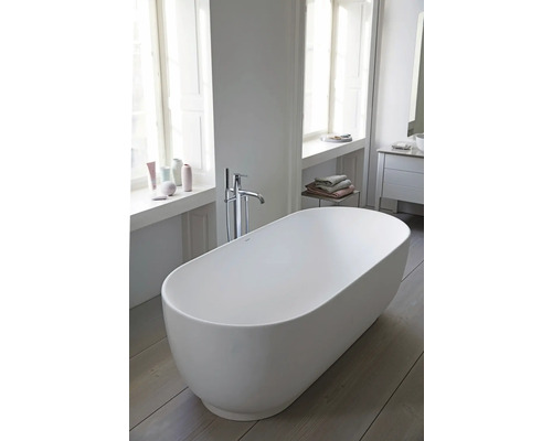 Baignoire îlot ovale dans une salle de bains moderne et lumineuse avec robinetterie au sol et parquet.