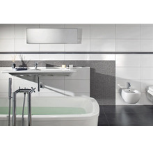 Modernes Badezimmer mit weißer Badewanne, wandhängendem Waschbecken und Bidet, grauen Mosaikfliesen und großflächigen weißen Wandfliesen.