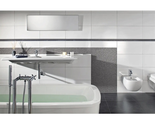 Modernes Badezimmer mit weißer Badewanne, wandhängendem Waschbecken und Bidet, grauen Mosaikfliesen und großflächigen weißen Wandfliesen.