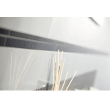 Nahaufnahme von weißen glänzenden Wandfliesen mit einer dunklen, strukturierten Bordüre.