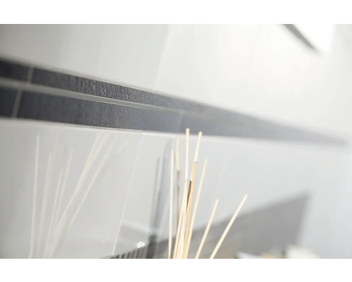 Nahaufnahme von weißen glänzenden Wandfliesen mit einer dunklen, strukturierten Bordüre.